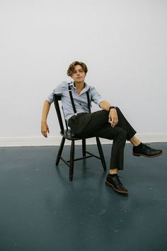 a young man sitting in a chair with his legs crossed and one foot on the ground