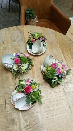 four plates with flowers on them sitting on a wooden table next to two cups and saucers