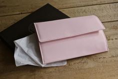 a pink purse sitting on top of a wooden table next to a black book and white tissue