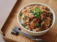 a small bowl filled with food on top of a wooden tray next to chopsticks