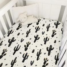 a white crib with black and white cactus print on the bedding, next to a teddy bear