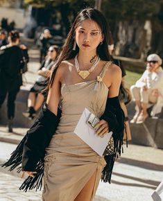 a woman walking down the street in a tan dress with fringes on her arms