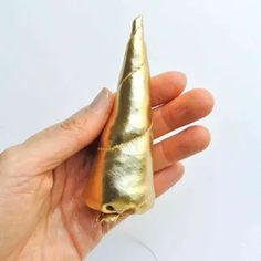 a hand holding a gold colored object in it's palm and the tip is shaped like a cone