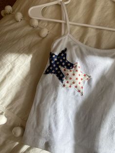 a white tank top with red, white and blue stars is laying on a bed