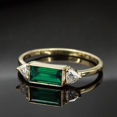 "Add a touch of elegance to your jewelry collection with this stunning Gold ring. The centerpiece of this ring is a beautiful Emerald baguette gemstone that is expertly paired with a pair of trillion cut Moissanites on either side, creating a striking contrast between the green of the Emerald and the clear of the Moissanites. The gemstones are set in line in a horizontal fashion, making it a perfect choice for stacking with other rings or wearing on its own. The Gold band adds an extra touch of Elegant Trillion Cut Gia Certified Emerald Ring, Elegant Gia Certified Trillion Cut Emerald Ring, Elegant Gia Certified Trillion Cut Ring, Elegant Vvs Clarity Trillion Cut Emerald Ring, Gia Certified Trillion Cut Emerald Wedding Ring, Gia Certified Trillion Cut Emerald Rings, Green Trillion Cut Diamond Ring, Classic Emerald Trillion Cut Ring, Gia Certified Trillion Cut Diamond Ring As Gift