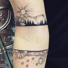 a woman's arm with two mountains and trees on the other side of it