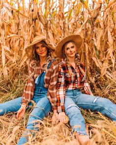 two women sitting in the middle of a corn field wearing overalls and hats with their arms around each other