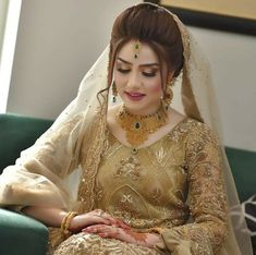 a woman sitting on top of a green couch wearing a wedding dress and jewelry in her hands