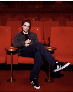 a man sitting on a red chair in front of a table with two chairs behind him