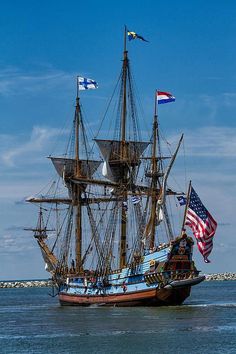 an old sailing ship in the water with flags flying from it's masts