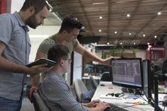 two men are looking at a computer screen while another man is holding a tablet in his hand