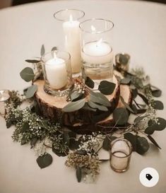 candles and greenery are arranged on top of a wooden slice for an elegant centerpiece