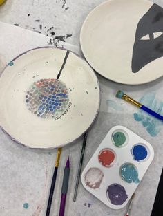 two plates with designs on them sitting next to paintbrushes and other art supplies