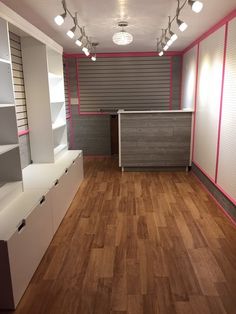 an empty room with white and pink walls, wooden flooring and shelving units