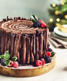 a cake with chocolate frosting and berries on the top is sitting on a wooden platter