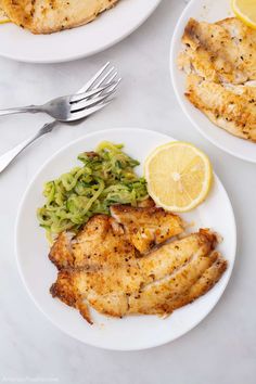 two white plates topped with chicken, broccoli and lemon wedges next to a fork