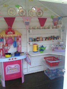 a play kitchen with lots of toys on the shelves and around it is pink, yellow and white