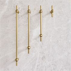 three brass - plated hooks hang on a marble wall, each holding two different sized handles