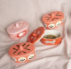 three small tins with designs on them are sitting on a white sheet next to some coins