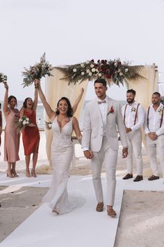 a bride and groom walking down the aisle with their wedding party on the beach behind them