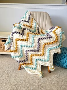 a crocheted blanket sitting on top of a chair next to a blue pillow