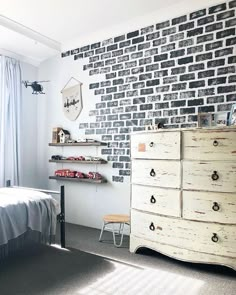 a bedroom with a brick wall and white dresser in front of the bed is shown