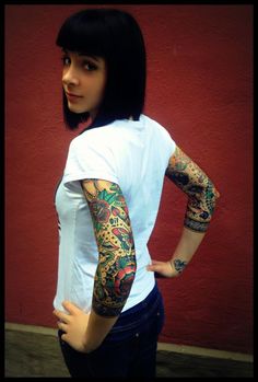 a woman with tattoos standing in front of a red wall and posing for the camera