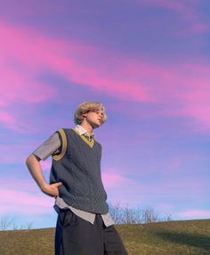 a young man standing on top of a grass covered field next to a pink sky