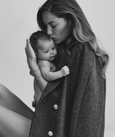 a woman holding a baby in her arms while wearing a coat and sitting on the floor