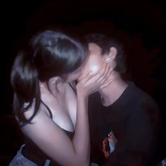 a man and woman kissing each other in front of a dark background with their hands covering their faces