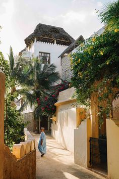 a woman walking down a street in front of a white and yellow building with palm trees