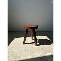 a small wooden stool sitting on top of a cement floor next to a white wall