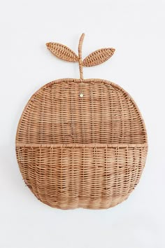 an apple shaped wicker basket hanging on the wall, with a leaf attached to it