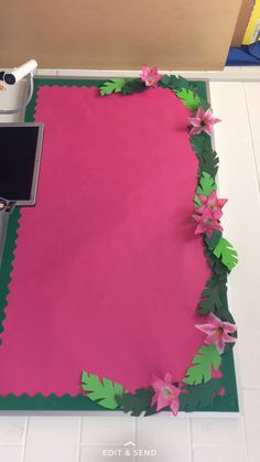 a pink sheet of paper with green leaves and flowers on it next to a computer