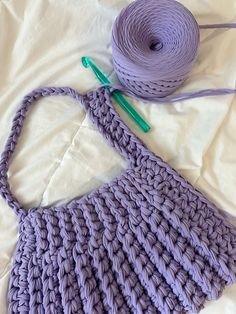 a crochet purse and yarn on a bed with white sheets, one purple