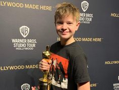 a young boy holding an award in front of a hollywood awards sign and posing for the camera