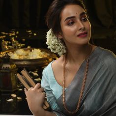 a woman in a sari is holding an open book and looking at the camera