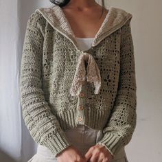 a woman wearing a green crochet cardigan with a hoodie over her shoulders