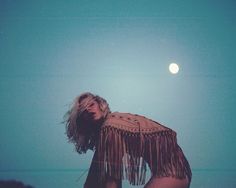 a woman with fringed hair standing on the beach at night, looking up into the sky