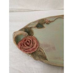 a ceramic dish with a rose on the center and leaves around it, sitting on a white surface