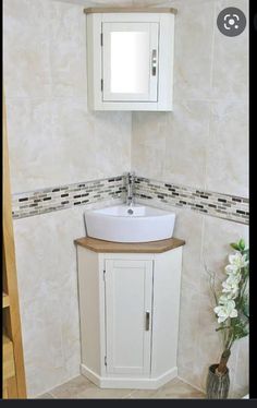 a white sink sitting under a bathroom mirror next to a wooden cabinet and vase with flowers