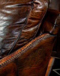 a brown leather chair with nailing on the arm