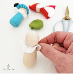 a hand is holding a small wooden doll next to some scissors and other crafting supplies