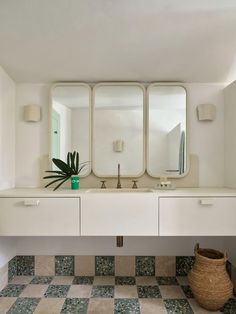 a bathroom with two sinks and three mirrors on the wall next to a basket filled with plants