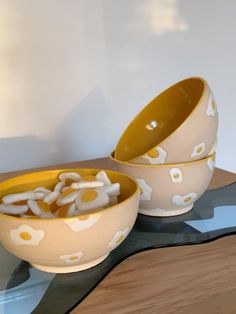 two yellow and white bowls filled with food on top of a wooden table next to a wall