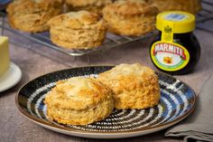 two biscuits on a plate next to some butter and other food items in the background