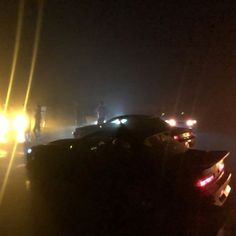 cars parked in the street at night with headlights on and foggy sky behind them