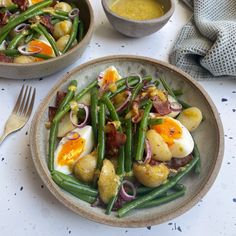 two bowls filled with green beans, potatoes and bacon