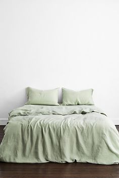 an unmade bed with green sheets and pillows on it in a white walled room