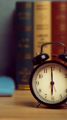 an alarm clock sitting on top of a wooden table in front of bookshelves